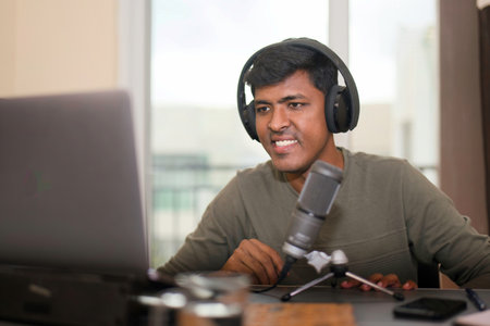 This iamge is about Focused man in headphones at desk with laptop and mic