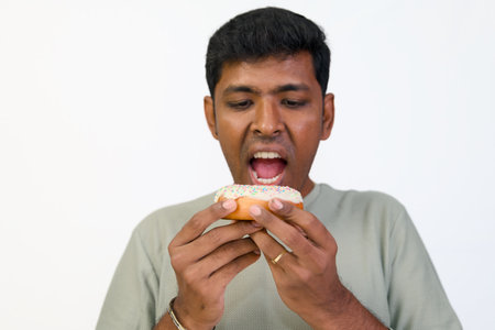 Man about to take a big bite of a delicious frosted donut with sprinkles.の写真素材