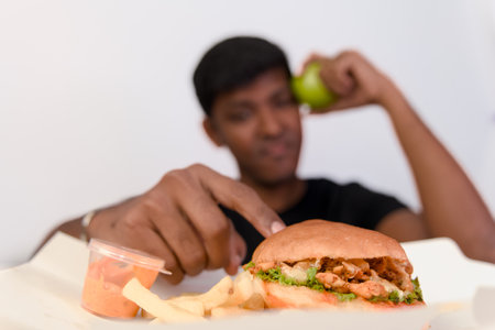 Healthy choice struggles? A juicy burger and fries tempt as a green apple hangs in the balance.の写真素材