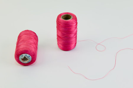 Two vibrant pink thread spools lie on a white background, a single strand trailing playfully. Ready...