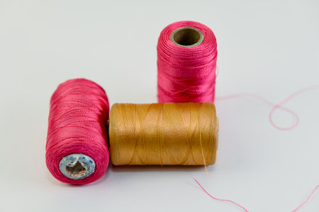 Vibrant pink & gold threads stand out against a clean white backdrop, ready for crafting & sewing...