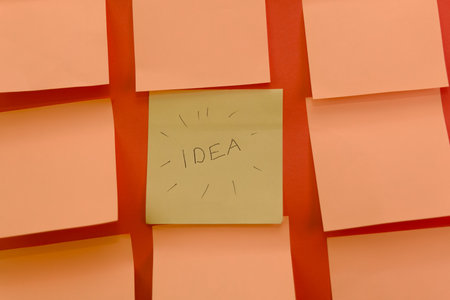 A single yellow sticky note stands out with "IDEA" scribbled across it, surrounded by blank orange notes.の写真素材