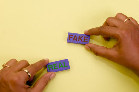 Hands hold wooden blocks spelling REAL and FAKE against a yellow background, symbolizing important...