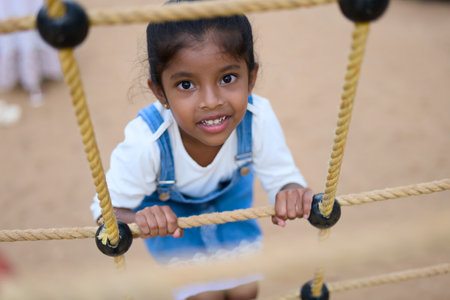 Adorable young girl smiles with joy while navigating a rope climbing frame at the playground.の写真素材