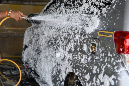A person is spraying foam and water on a gray vehicle at a car wash station, actively cleaning it...