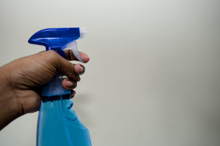 Ready to clean! Close-up of a hand holding a blue spray bottle against a neutral background.の写真素材