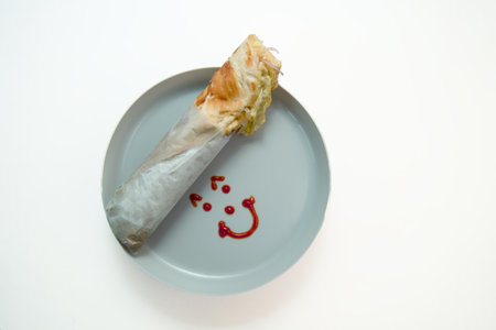 A fresh, tasty wrap placed on a grey plate with a cute ketchup smiley face design, perfect for quick...