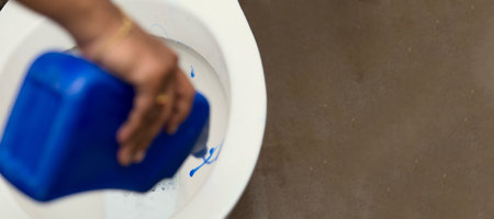 Hand pours blue cleaning fluid into a toilet bowl, ready for a deep clean.