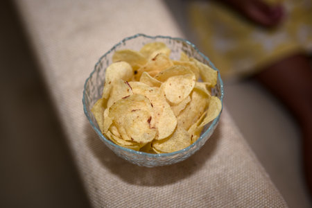 This little girl enjoys the satisfying crunch of a delicious potato chip, eyes sparkling with...