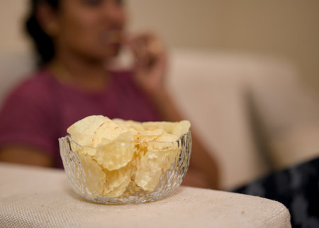Bowl of potato chips with a blurry woman snacking in the background.