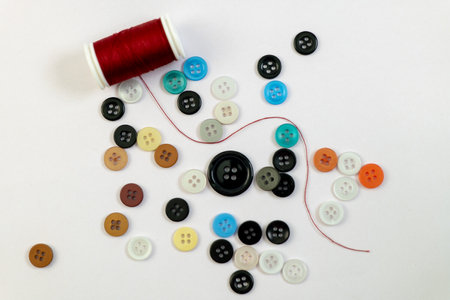A vibrant scattering of colorful buttons and red thread on a clean white background, ready for...
