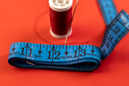 Red thread, needle, and blue measuring tape on vibrant red. Perfect for tailoring, fashion, and DIY projects.の写真素材