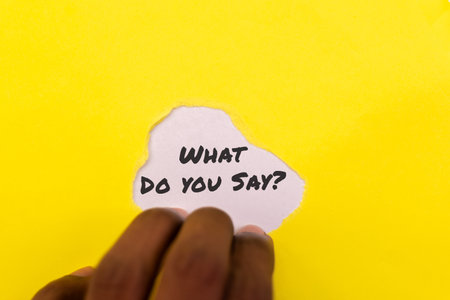 Hand reveals hidden message on bright yellow background. Intrigue, curiosity, and question mark. What's the answer?の写真素材