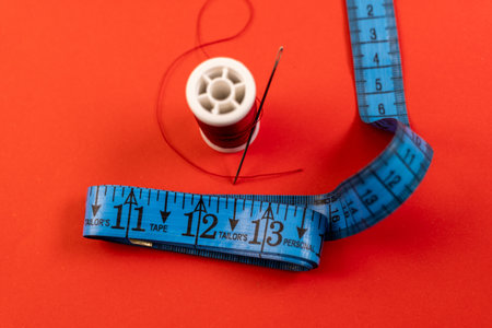spool of thread with needle and measuring tape on a red background