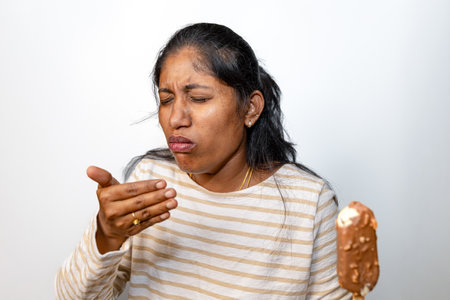 Woman experiencing a brain freeze while eating a chocolate ice cream bar.  Perfect for summer, dessert, or sensitivity themes.の写真素材