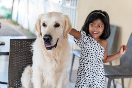 A young girl happily pets her gentle Golden Retriever companion on a sunny day.