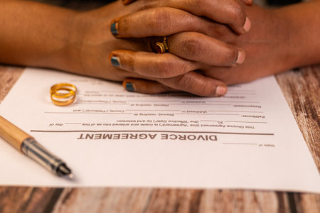 Hands clasped over a divorce agreement, wedding rings nearby.  A difficult choice, ending a marriage.の写真素材