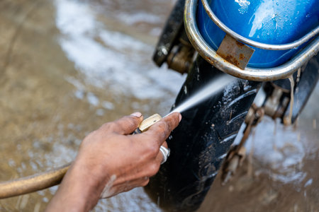 Close-up of hand washing a muddy motorcycle tire with water hose. Cleaning, maintenance, and care concept.の写真素材