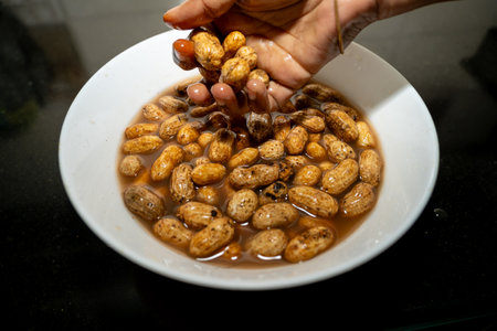Hands gently rinsing raw peanuts in water, preparing them for cooking. A close-up of a culinary tradition.の写真素材