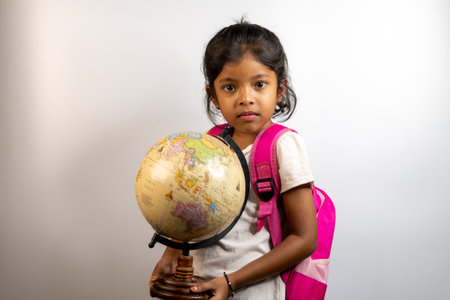 Curious young girl ready for adventure, holding a globe and wearing a pink backpack.の写真素材
