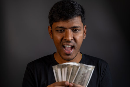 Shocked young man stares in disbelief at Indian Rupees. Perfect for finance, wealth, and surprise concepts.の写真素材