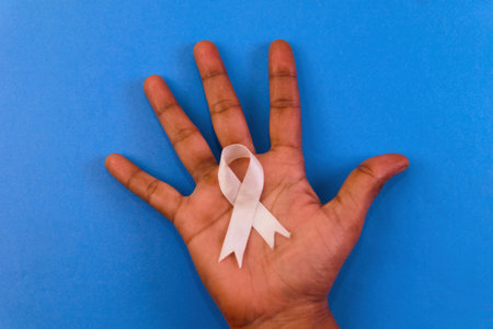 A hand holding a ribbon that says breast cancer awareness The ribbon is white and is in the middle...