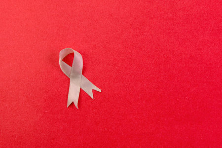 A gray ribbon rests on a vibrant red background, symbolizing awareness and support for various...