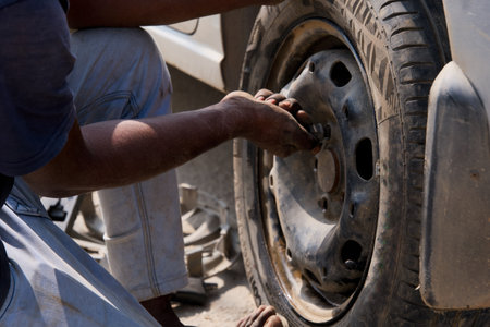 This image shows a close-up view of a person working on a car tire, using a tool to tighten or loosen the lug nuts on the wheelの写真素材