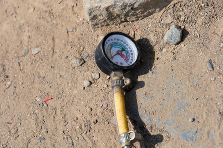 This image shows a close-up of a pressure gauge lying on sandy ground.