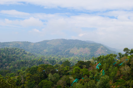 A picturesque view of lush, green hills covered with dense forests under a partly cloudy sky. The...