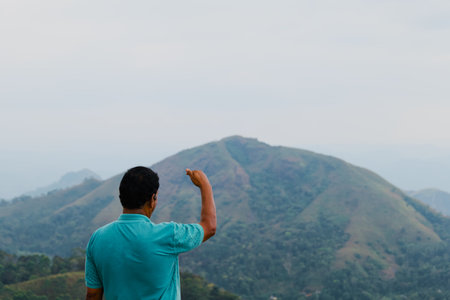 Back view of a man standing on top of a mountain and raising his handの写真素材