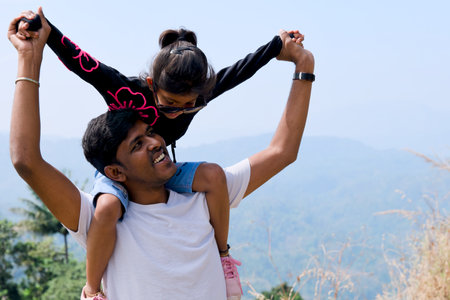 Father carrying his daughter on his shoulders at the top of the mountain