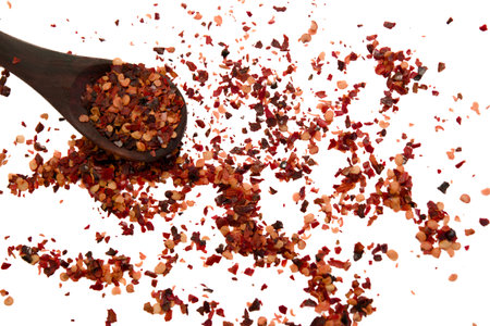 A wooden spoon lifts red chili flakes over a colorful spread on a white surface.の写真素材