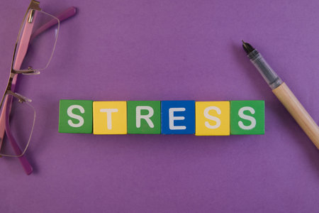Colorful blocks spell stress with glasses and a pen on a vibrant purple background, highlighting a...