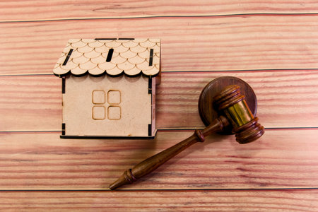 A wooden house model sits beside a gavel, representing legal matters in real estate during a focused discussion.の写真素材