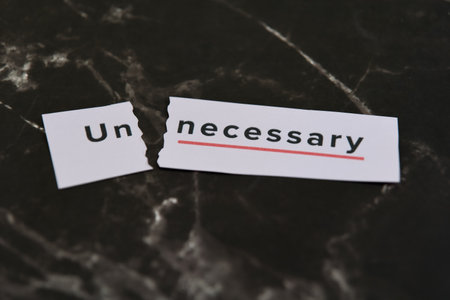 Torn paper pieces display the word unnecessary on a dark marble surface in a creative setup.