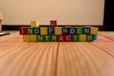 Colorful blocks arranged to spell out independent contractor on a wooden tabletop in an office setting.の写真素材