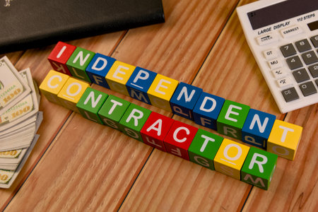 Colorful blocks say independent contractor on a wooden table with cash and a calculator, symbolizing...