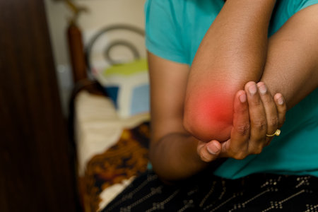 A person is applying pressure on their elbow for pain relief in a comfortable home setting.の写真素材