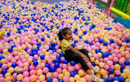 Young girl enjoying herself while sitting in a vibrant ball pit filled with colorful plastic balls...