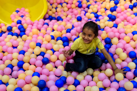 A young girl enjoys playing in a ball pit filled with pink and blue balls at a vibrant indoor...