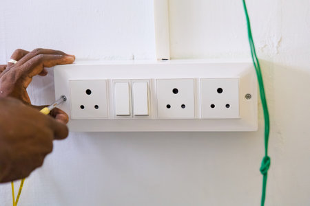 A skilled electrician works on installing electrical outlets and switches on a white wall indoors...