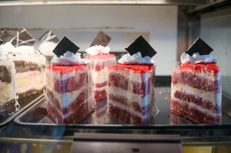 Colorful red velvet cake slices with cream frosting sit behind glass in a bakery, enticing customers with sweetness.の写真素材