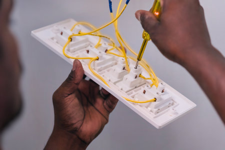 Hands are connecting yellow wires to several electrical outlets on a white panel. The work is taking place indoors.の写真素材