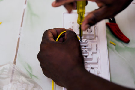 Person uses a screwdriver to connect electrical wires in a home setting.
