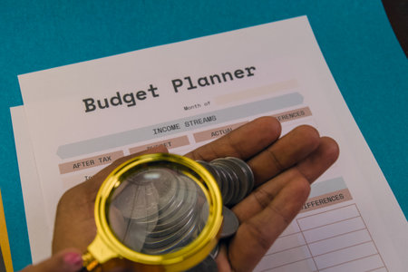 A hand holding coins above a budget planner, focusing on financial organization and planning for the month ahead.の写真素材