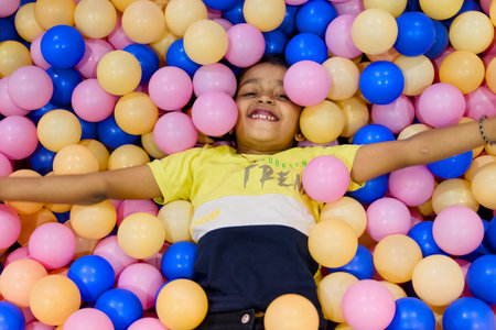 Child smiles while lying in a vibrant ball pit, surrounded by blue and pink plastic balls, enjoying carefree playtime.の写真素材