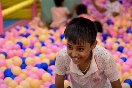 A child plays happily in a colorful ball pit with pink and blue balls, surrounded by friends indoors.の写真素材