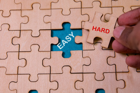 A hand placing a puzzle piece labeled hard into a blue puzzle missing a piece labeled easy.の写真素材