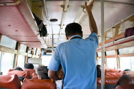 A bus conductor interacts with seated passengers during a busy commute in a city setting.の写真素材